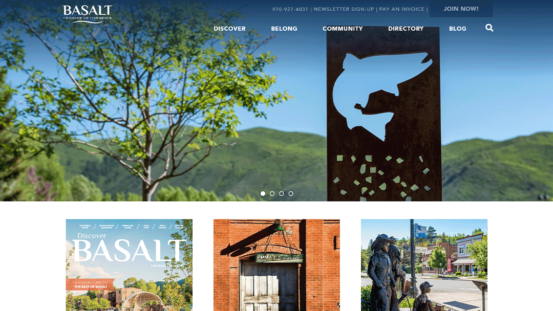 A scenic view of Basalt, Colorado, featuring lush green mountains and a metal sculpture with a fish cutout in the foreground. The image is part of the Basalt Chamber of Commerce website, promoting local attractions and community engagement.