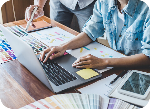website-design Two people collaborating at a desk with a laptop, color swatches, design sketches, and a tablet, suggesting a creative website design project